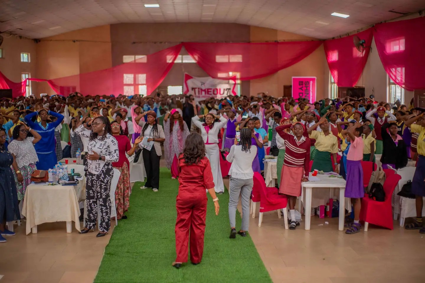 Teenage girls and mentors seated in a hall with pink drapes and a green central aisle at Timeout with the Peerless Ladies